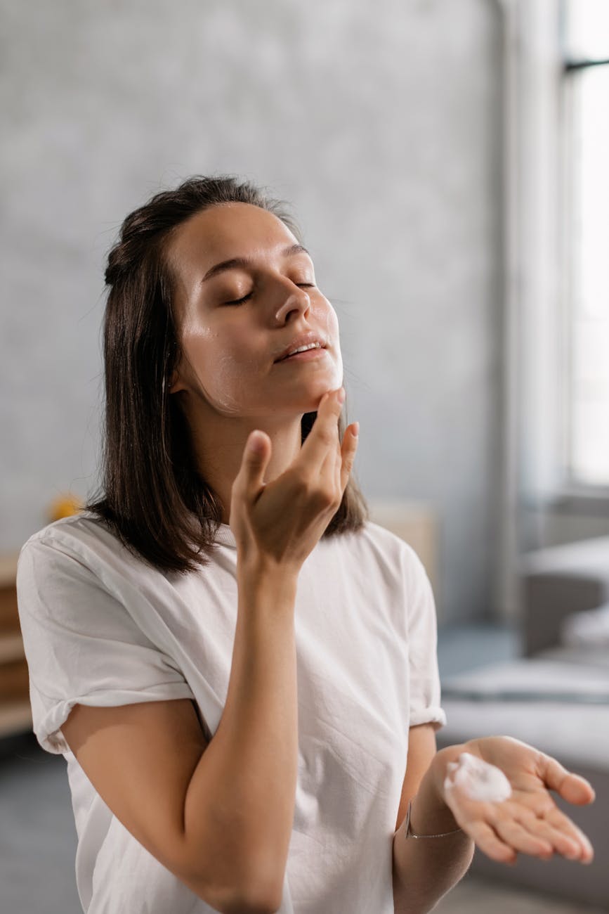a woman in white t shirt applying cream on chin