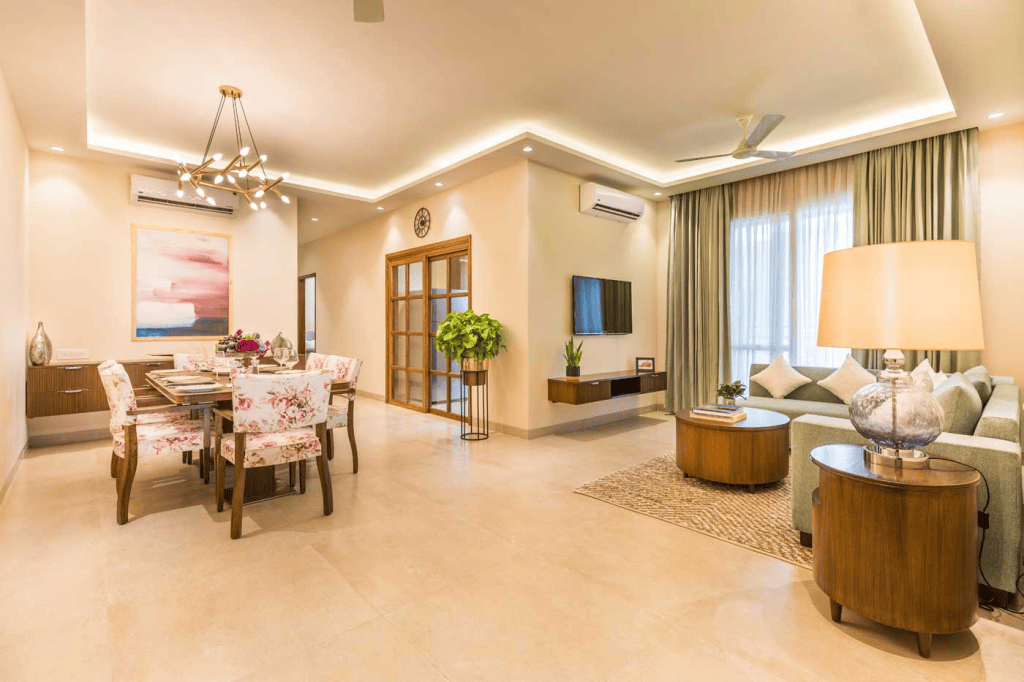 A modern senior living apartment with a spacious living and dining area, featuring floral-patterned furniture, a cozy sofa, a stylish chandelier, and large windows allowing natural light.