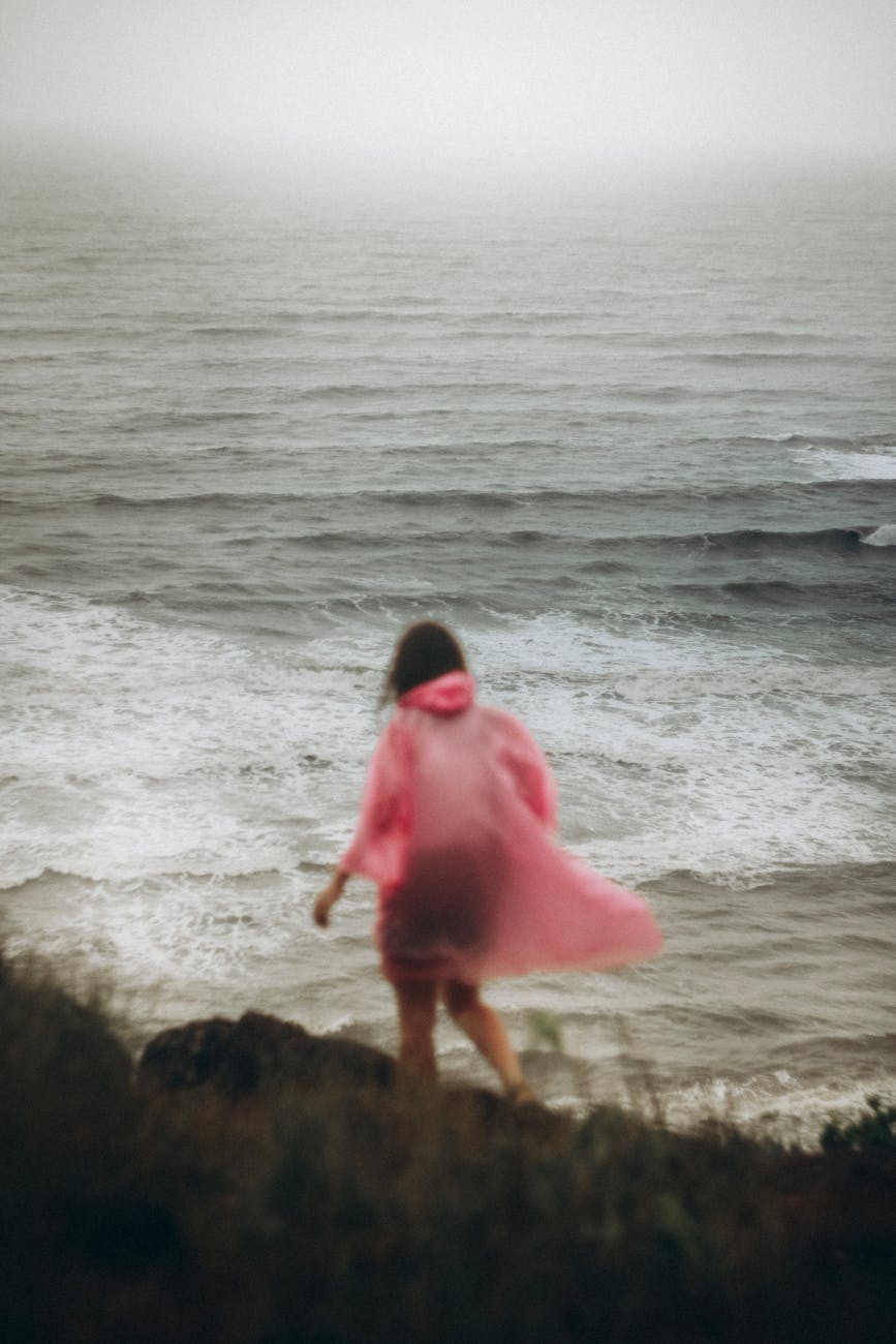 woman in pink raincoat overlooking misty ocean