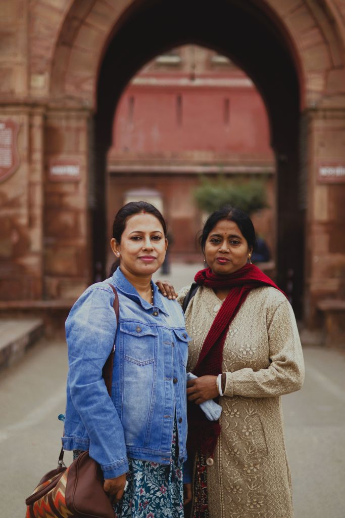 Two women standing together under a large archway, with one wearing a denim jacket and the other dressed in a traditional outfit.