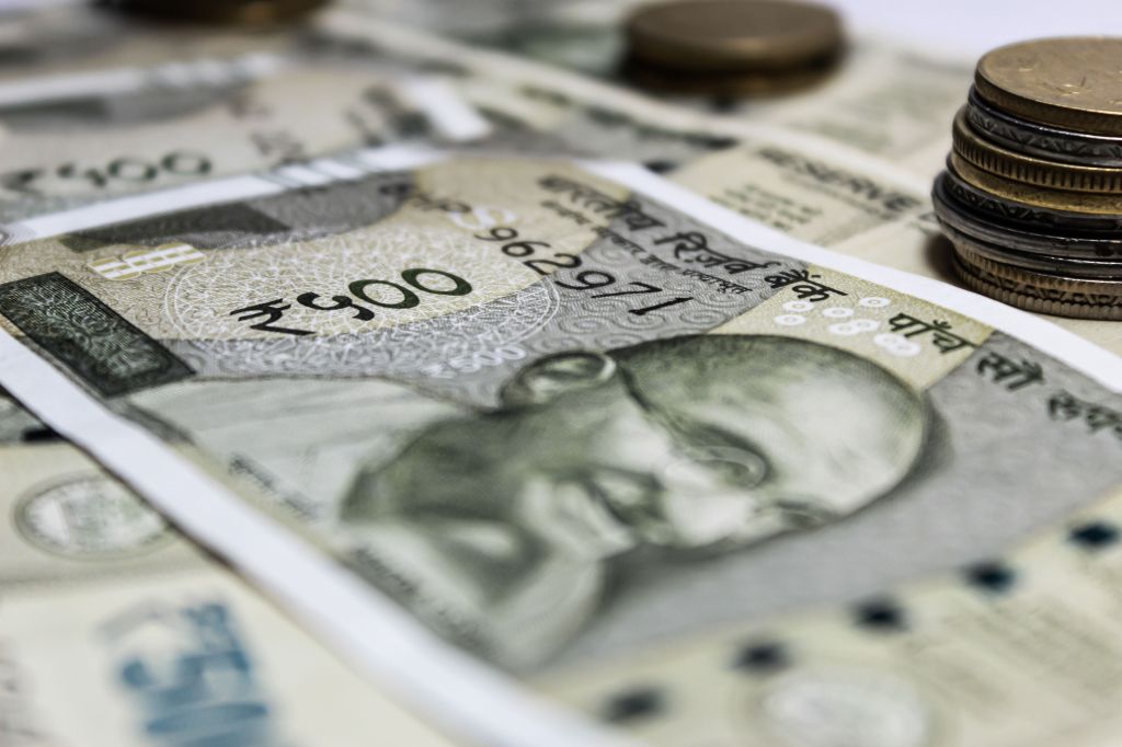 Close-up of Indian currency notes featuring a portrait of Mahatma Gandhi with coins in the background.
