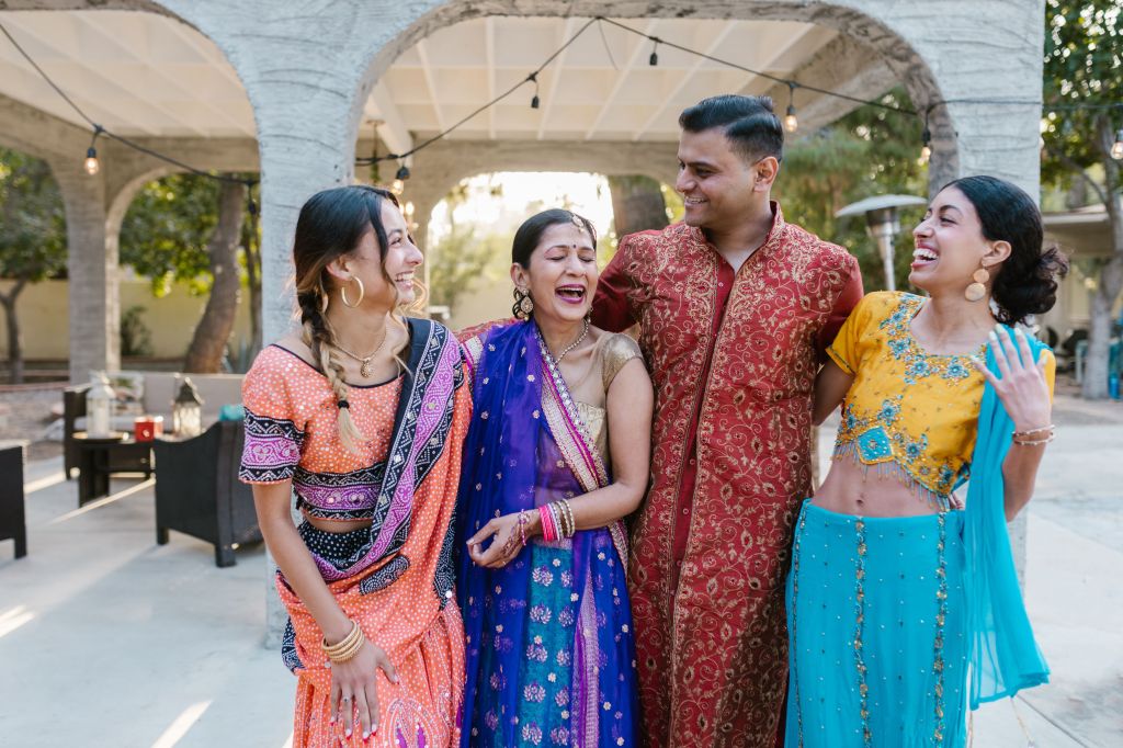 Four friends laughing and celebrating in traditional Indian attire outdoors.