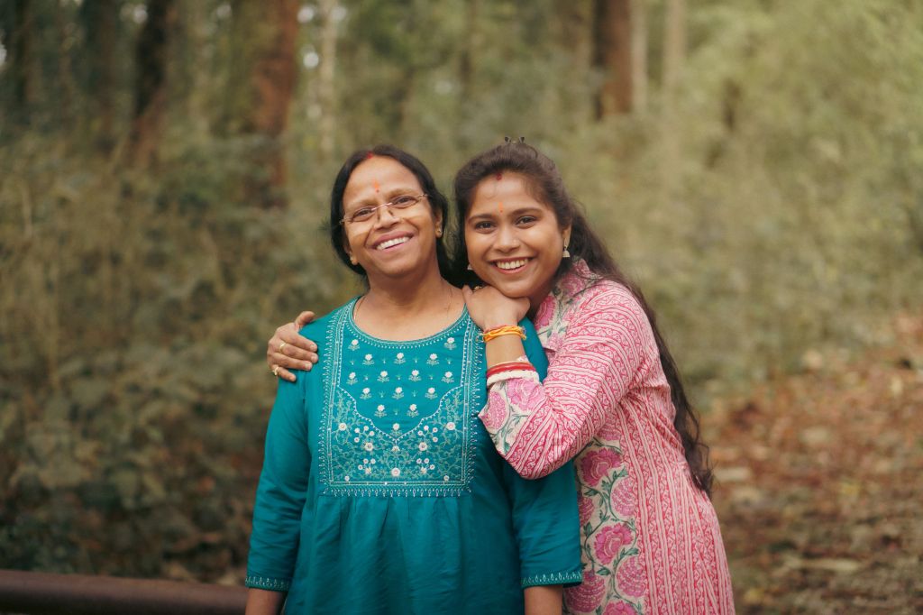 A smiling woman and her daughter pose together in a forested area, showcasing a warm and loving relationship.