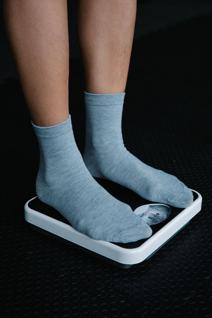 A person standing on a weighing scale, wearing gray socks, revealing only the lower legs.