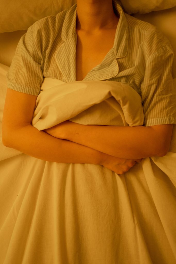 A person wearing a striped pajama top is lying in bed, wrapped in a white blanket with arms crossed over their chest.